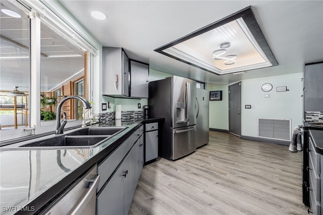 kitchen with sink, light hardwood / wood-style flooring, appliances with stainless steel finishes, gray cabinetry, and a tray ceiling