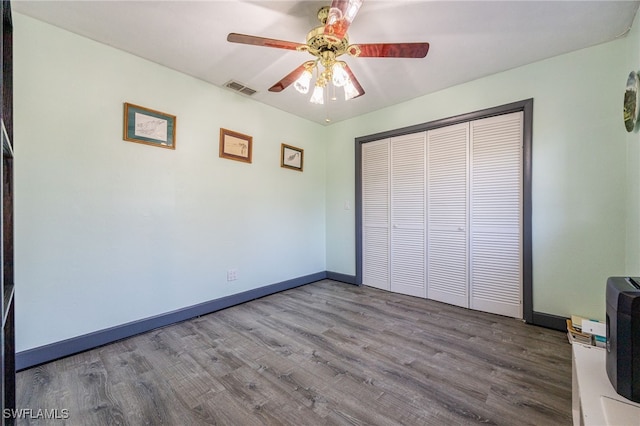 unfurnished bedroom featuring baseboards, visible vents, a ceiling fan, wood finished floors, and a closet