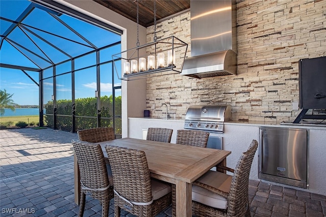 view of patio with sink, exterior kitchen, grilling area, glass enclosure, and a water view