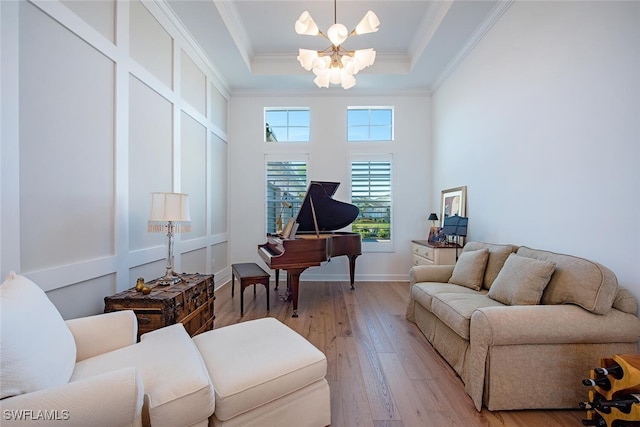 living area with crown molding, a chandelier, a raised ceiling, and light hardwood / wood-style floors