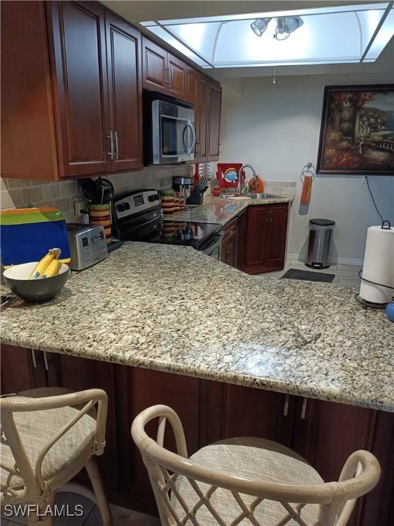 kitchen featuring a breakfast bar, sink, light stone counters, appliances with stainless steel finishes, and kitchen peninsula