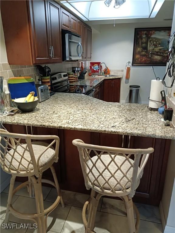 kitchen featuring a breakfast bar, sink, light stone counters, appliances with stainless steel finishes, and kitchen peninsula