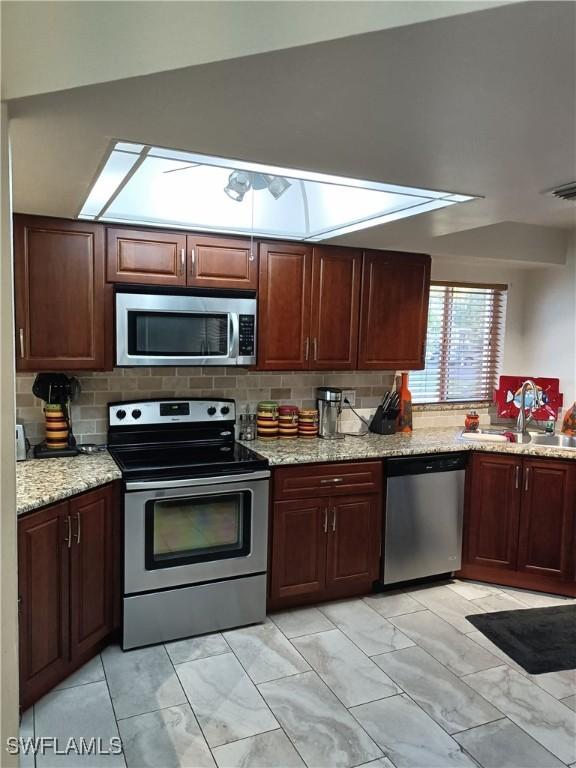 kitchen with sink, backsplash, stainless steel appliances, and light stone countertops