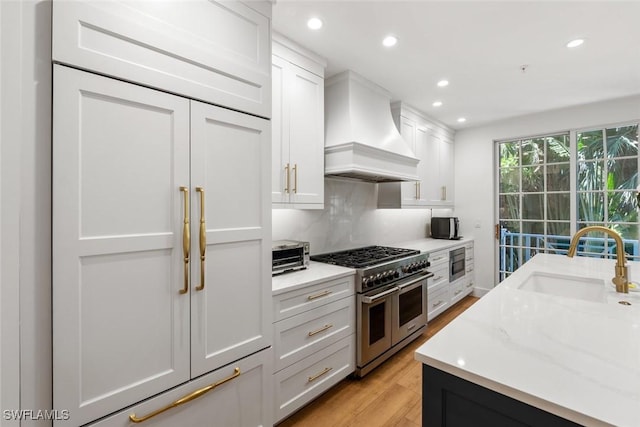 kitchen featuring premium range hood, light stone countertops, built in appliances, and white cabinets