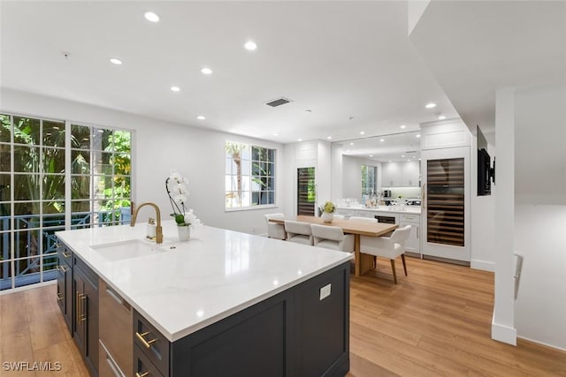 kitchen featuring stainless steel dishwasher, an island with sink, sink, and light wood-type flooring