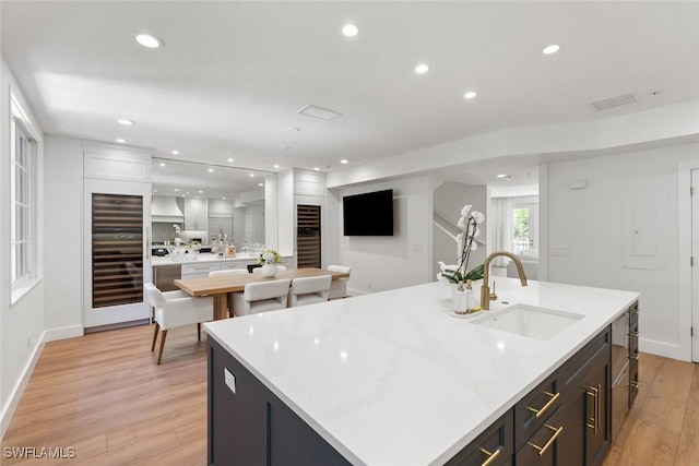 kitchen with light stone counters, sink, light hardwood / wood-style flooring, and a center island with sink