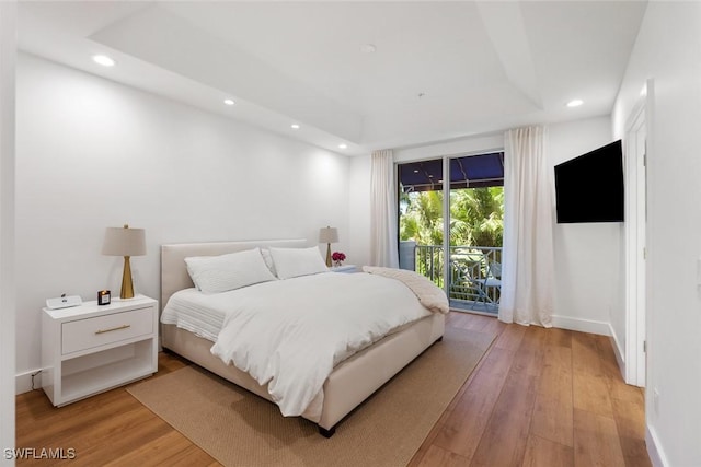 bedroom with a tray ceiling, light wood-type flooring, and access to outside