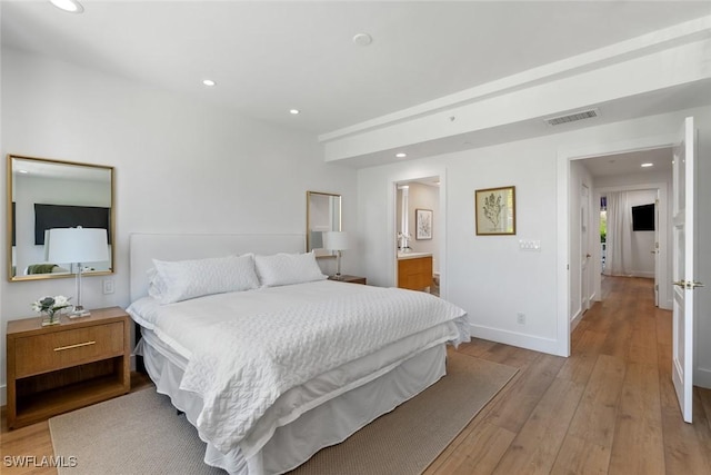 bedroom with connected bathroom and light hardwood / wood-style floors