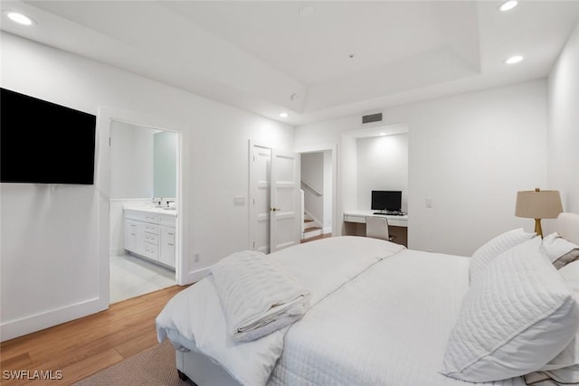 bedroom with sink, a tray ceiling, ensuite bathroom, and light wood-type flooring