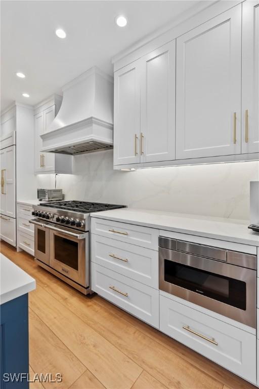 kitchen featuring light hardwood / wood-style flooring, built in appliances, custom exhaust hood, and white cabinets