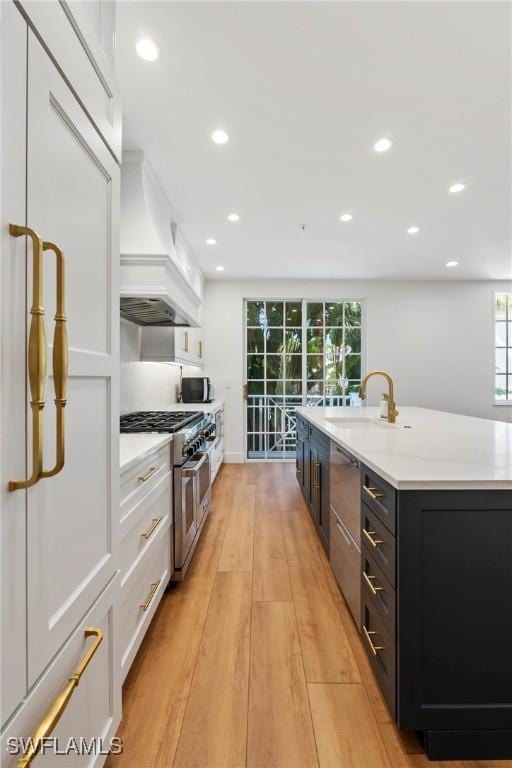 kitchen with sink, white cabinets, a kitchen island with sink, stainless steel appliances, and light wood-type flooring