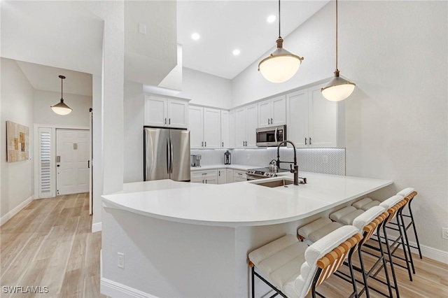 kitchen featuring a sink, a kitchen breakfast bar, appliances with stainless steel finishes, light wood finished floors, and tasteful backsplash