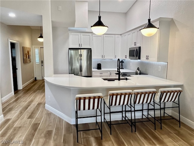 kitchen featuring a peninsula, a sink, light wood-style floors, appliances with stainless steel finishes, and tasteful backsplash