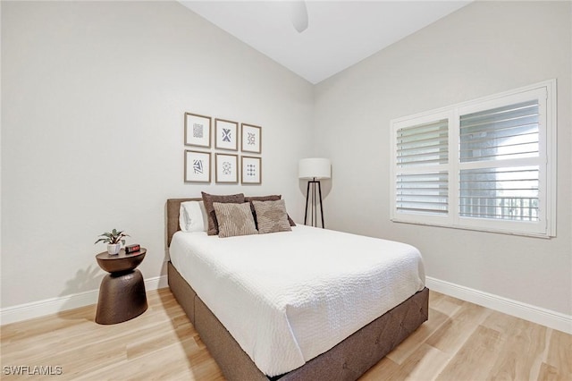 bedroom with vaulted ceiling, ceiling fan, light wood-style flooring, and baseboards