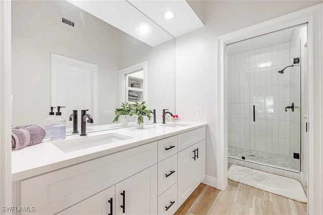 full bathroom with double vanity, wood finished floors, a stall shower, and a sink