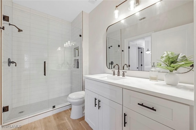 bathroom featuring visible vents, toilet, wood finished floors, vanity, and a shower stall