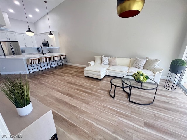 living room with light wood finished floors, recessed lighting, a high ceiling, and baseboards