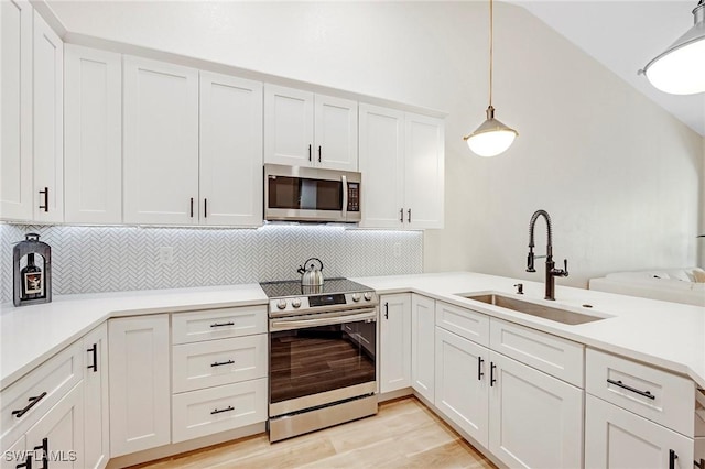 kitchen featuring light wood-style flooring, a sink, white cabinets, vaulted ceiling, and appliances with stainless steel finishes