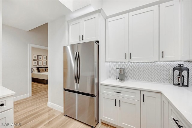 kitchen with decorative backsplash, light wood-style flooring, freestanding refrigerator, light countertops, and white cabinetry