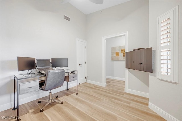 office space featuring a towering ceiling, light wood-style flooring, visible vents, and baseboards