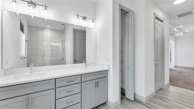 full bath featuring a tile shower, a sink, visible vents, and baseboards