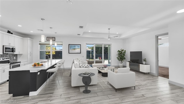 living area with a tray ceiling, a wealth of natural light, and recessed lighting