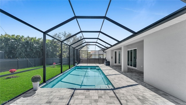 view of swimming pool featuring a patio, glass enclosure, a fenced backyard, a lawn, and a fenced in pool