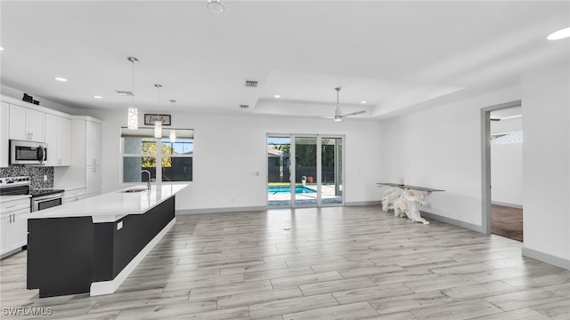 kitchen featuring tasteful backsplash, a raised ceiling, light countertops, stainless steel appliances, and a sink