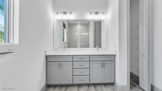 full bath featuring a tile shower, a spacious closet, double vanity, and a sink