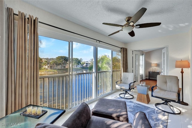 tiled living room featuring ceiling fan, a textured ceiling, and a water view