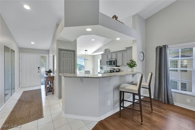 kitchen with gray cabinets, appliances with stainless steel finishes, a kitchen bar, kitchen peninsula, and light stone countertops