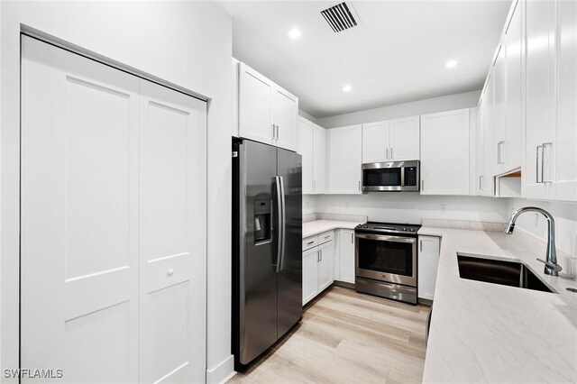 kitchen with stainless steel appliances, sink, white cabinets, and light hardwood / wood-style flooring