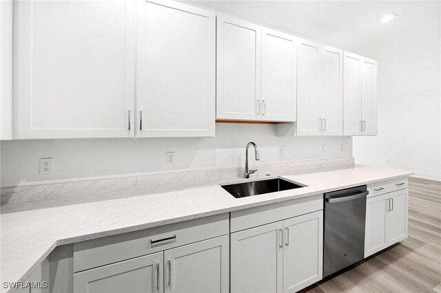 kitchen featuring white cabinetry, dishwasher, sink, light stone counters, and light hardwood / wood-style flooring