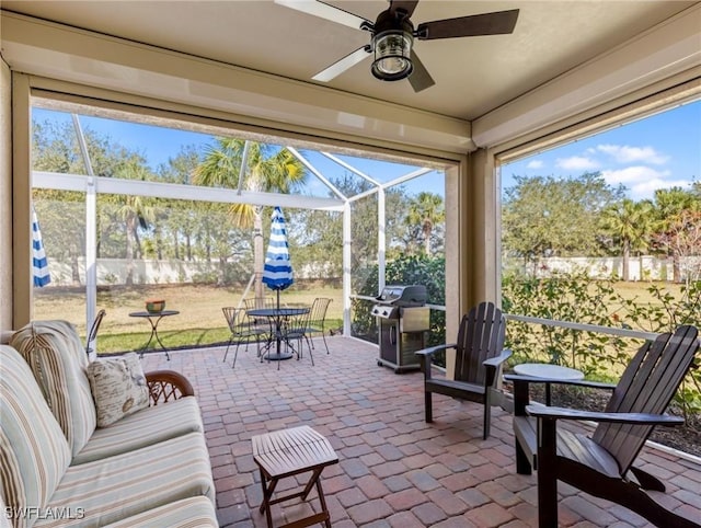 view of patio with area for grilling, ceiling fan, and glass enclosure