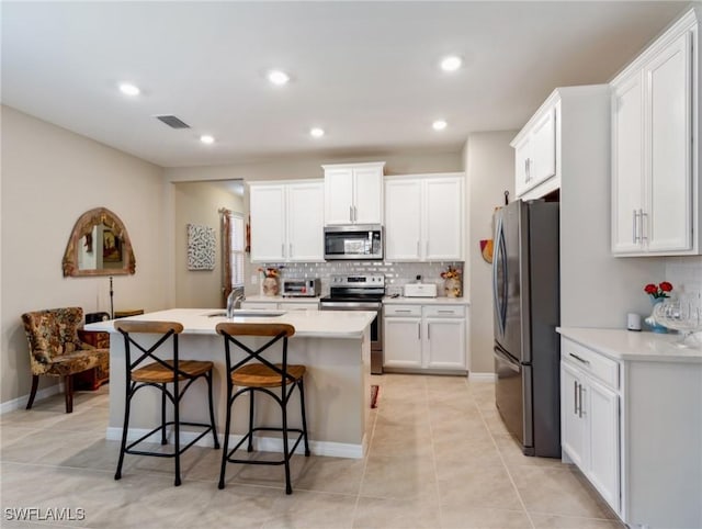 kitchen with a breakfast bar, appliances with stainless steel finishes, white cabinetry, an island with sink, and decorative backsplash