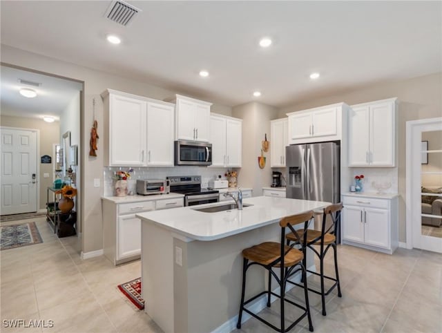 kitchen with sink, white cabinetry, stainless steel appliances, tasteful backsplash, and an island with sink