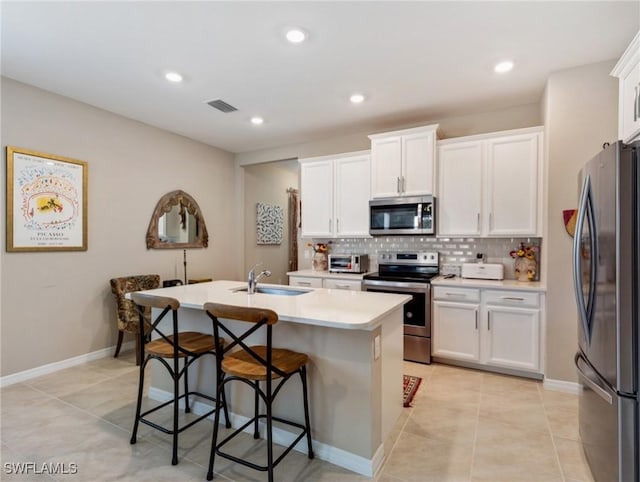 kitchen with visible vents, white cabinets, appliances with stainless steel finishes, a kitchen island with sink, and backsplash