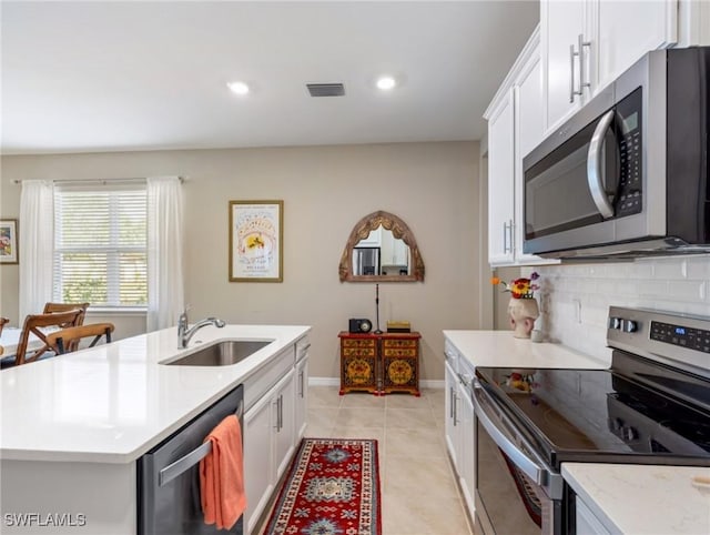 kitchen featuring appliances with stainless steel finishes, sink, white cabinets, decorative backsplash, and a kitchen island with sink