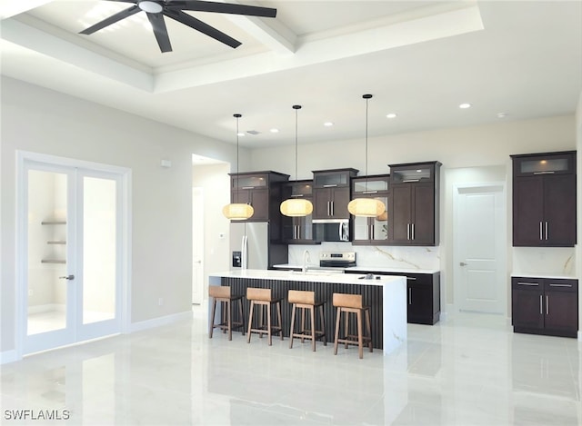 kitchen featuring decorative light fixtures, a kitchen island with sink, dark brown cabinetry, stainless steel appliances, and french doors