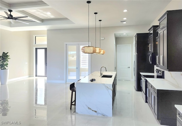 kitchen with appliances with stainless steel finishes, sink, hanging light fixtures, light stone counters, and a center island with sink