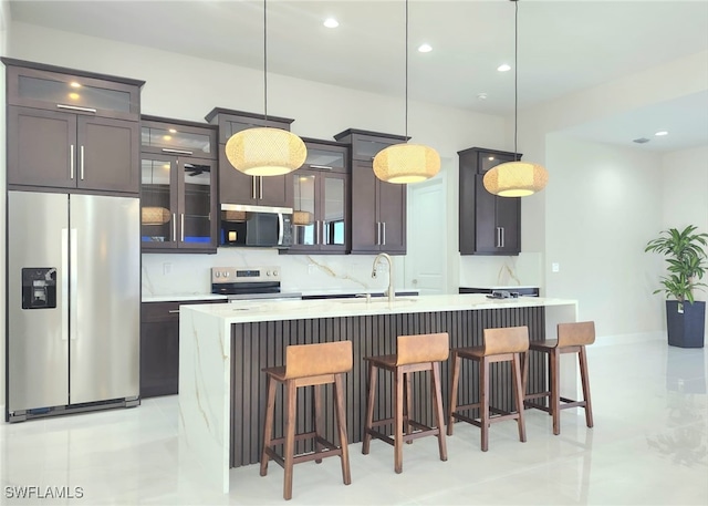 kitchen featuring sink, tasteful backsplash, hanging light fixtures, appliances with stainless steel finishes, and a kitchen island with sink