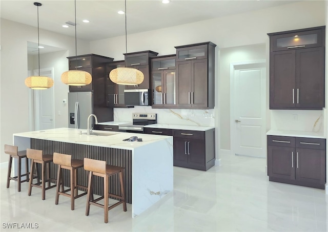 kitchen featuring sink, appliances with stainless steel finishes, a kitchen island with sink, hanging light fixtures, and dark brown cabinets