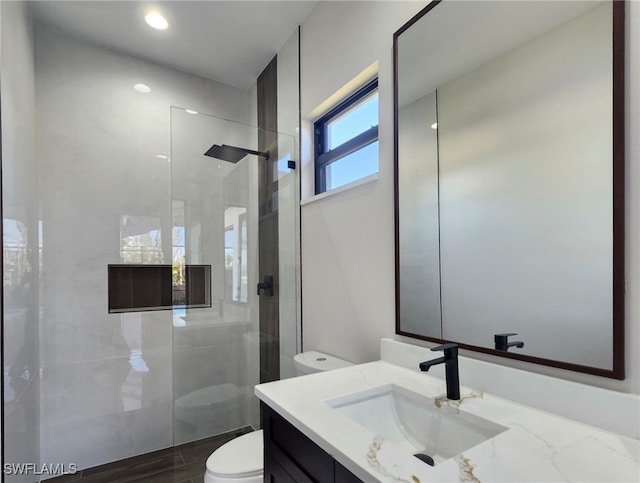 bathroom with vanity, tiled shower, and toilet