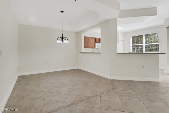 unfurnished room with light tile patterned flooring, a chandelier, and a tray ceiling