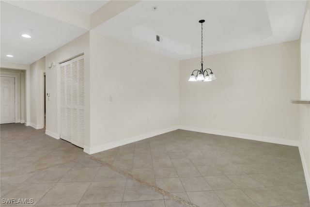 tiled spare room featuring a raised ceiling and a notable chandelier