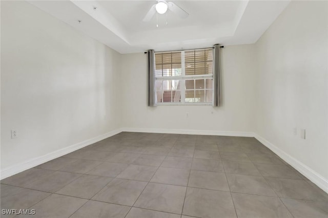 tiled empty room with ceiling fan and a raised ceiling