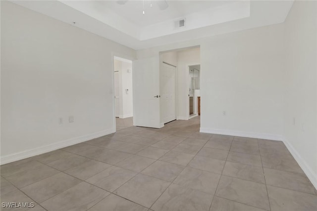 spare room with ceiling fan, a raised ceiling, and light tile patterned floors