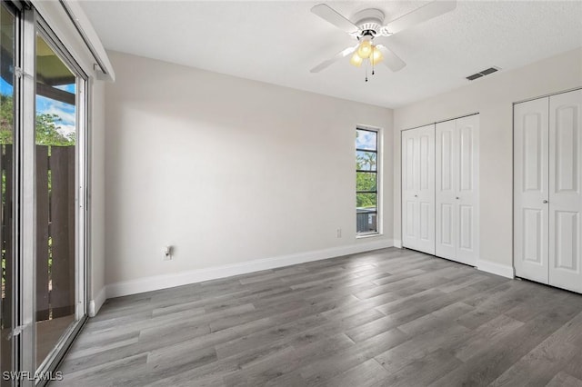 unfurnished bedroom featuring baseboards, visible vents, wood finished floors, access to outside, and multiple closets