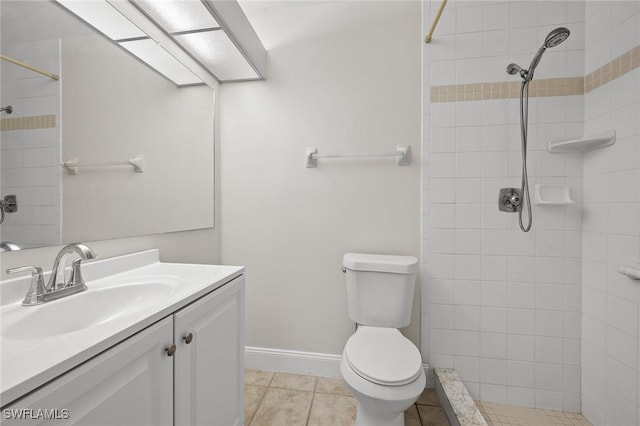 bathroom with toilet, a tile shower, vanity, tile patterned flooring, and baseboards