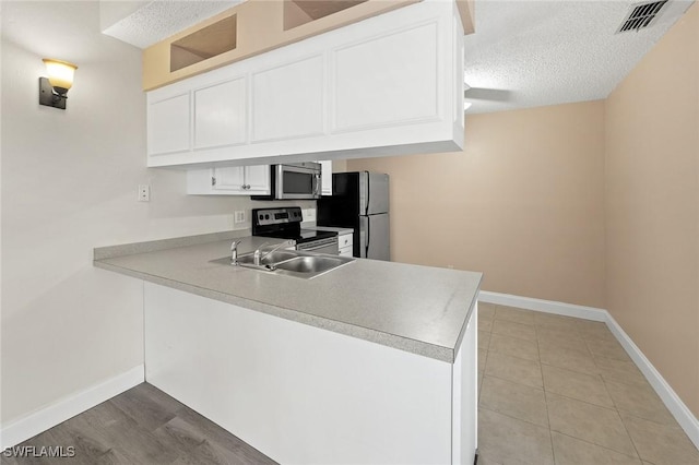 kitchen featuring a textured ceiling, a peninsula, a sink, white cabinetry, and appliances with stainless steel finishes